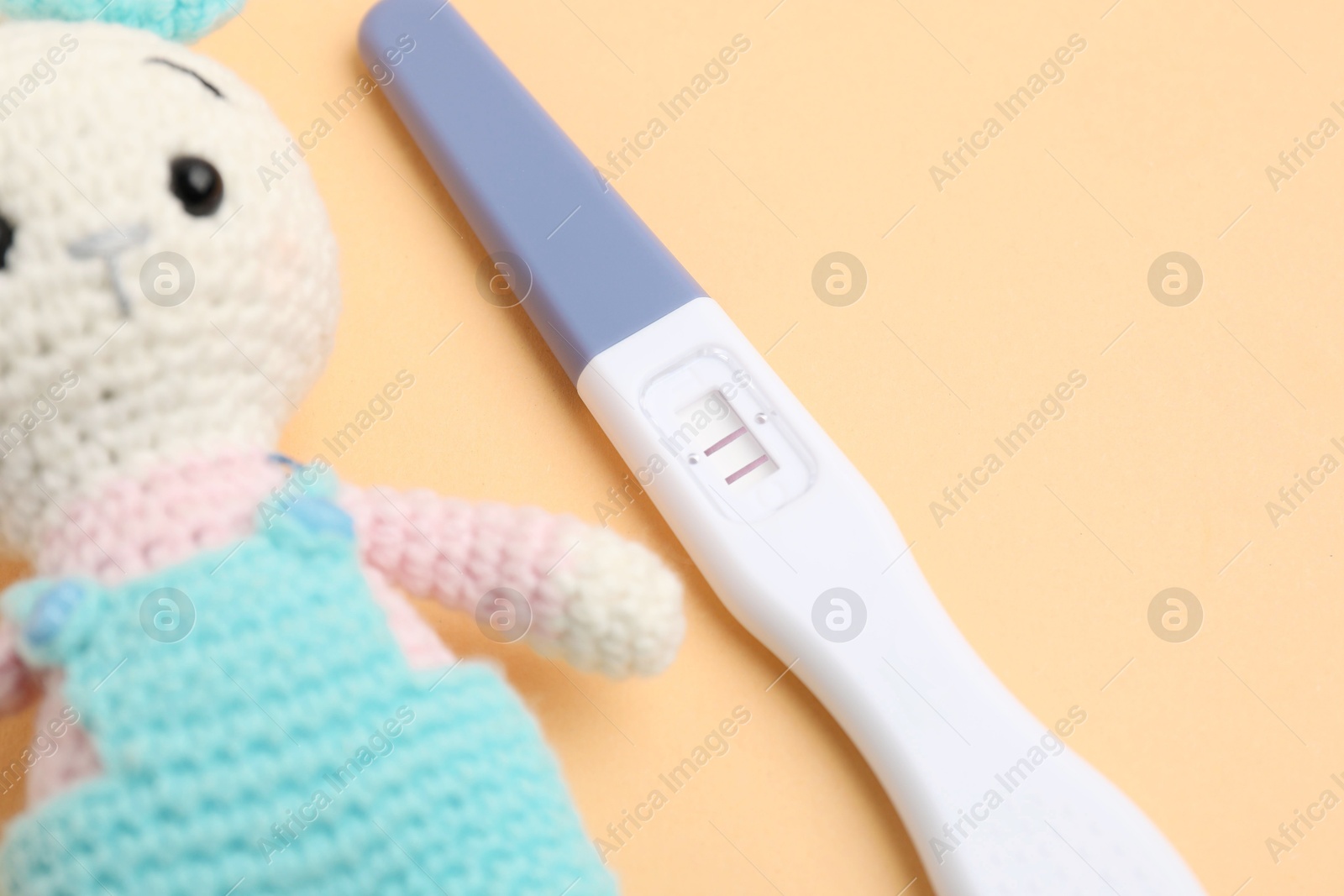 Photo of Pregnancy test and toy bunny on pale orange background, closeup