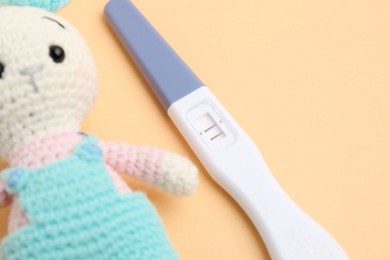 Photo of Pregnancy test and toy bunny on pale orange background, closeup