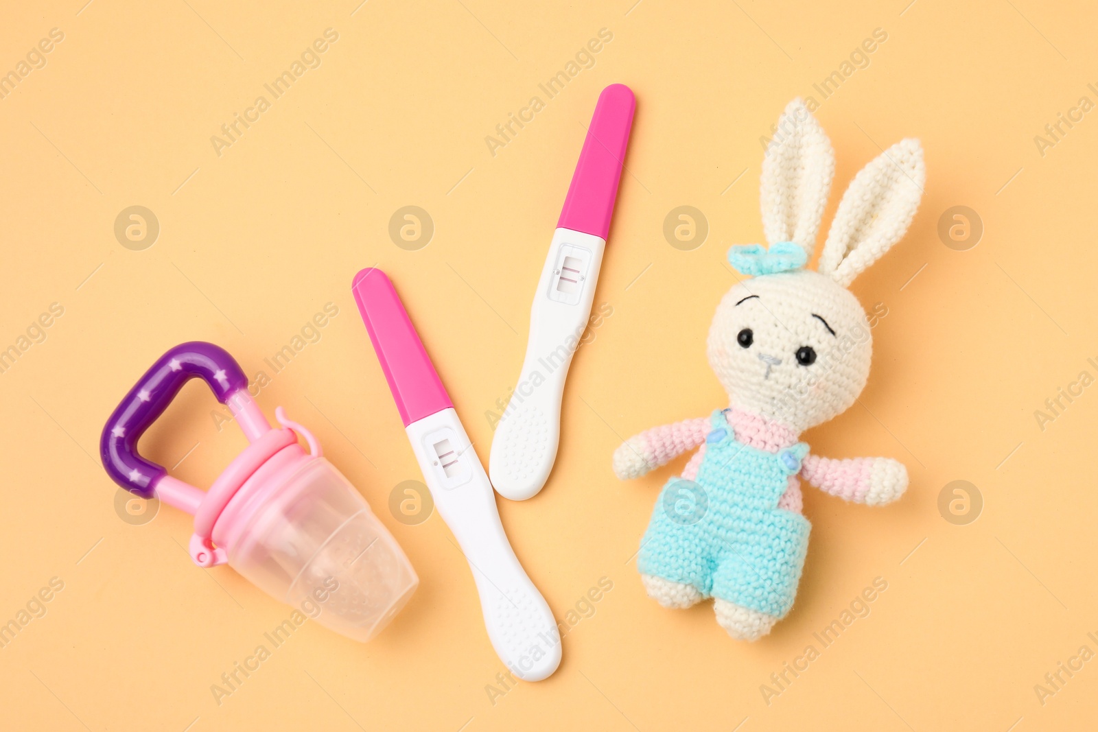 Photo of Pregnancy tests, nibbler and toy bunny on pale orange background, top view