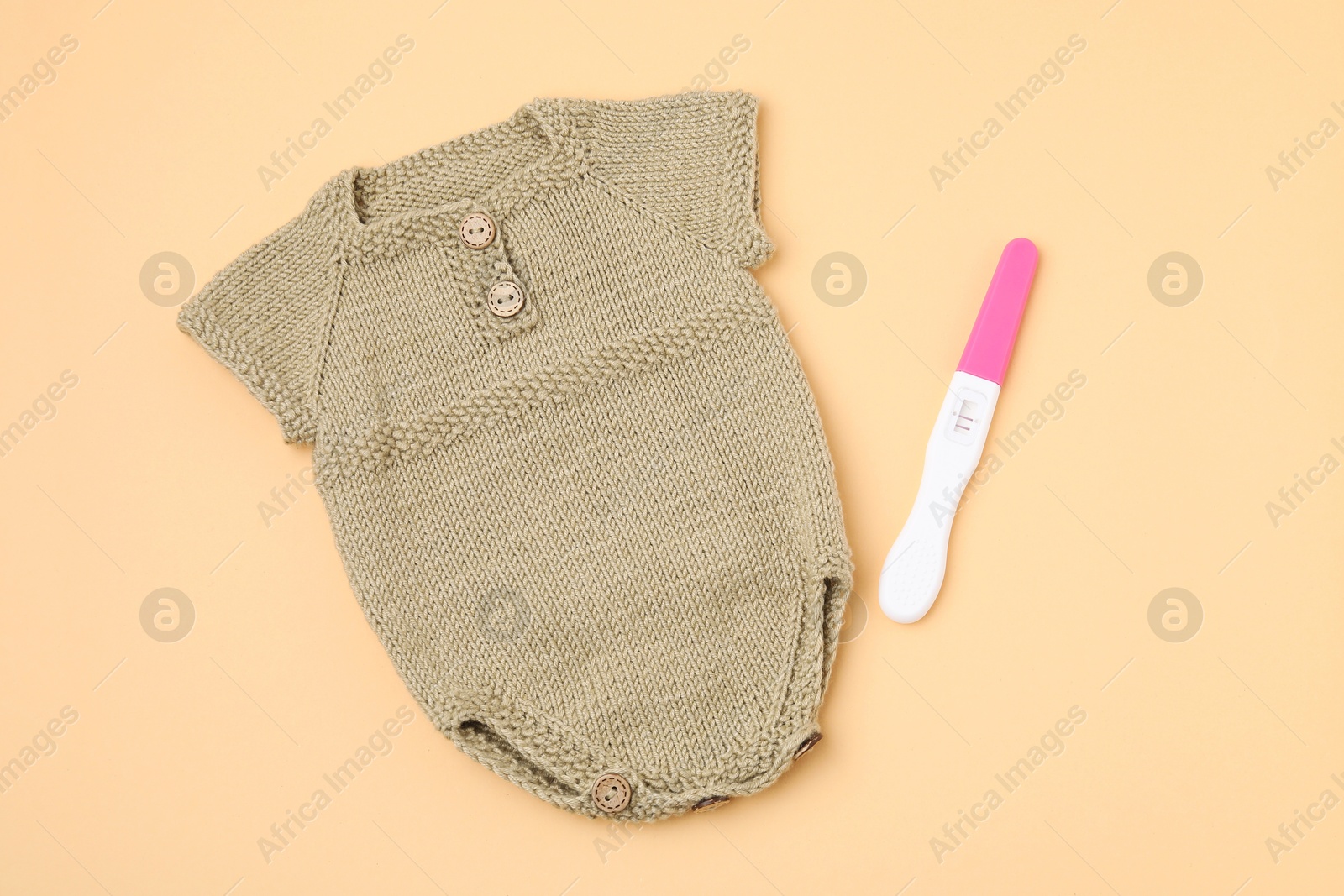 Photo of Pregnancy test and baby clothes on pale orange background, top view