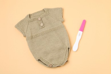 Photo of Pregnancy test and baby clothes on pale orange background, top view