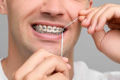 Man with braces cleaning teeth using dental floss on grey background, closeup