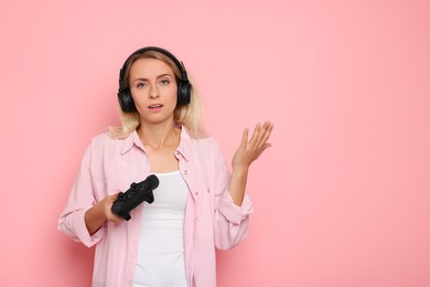 Photo of Unhappy woman in headphones playing video games with controller on pink background, space for text