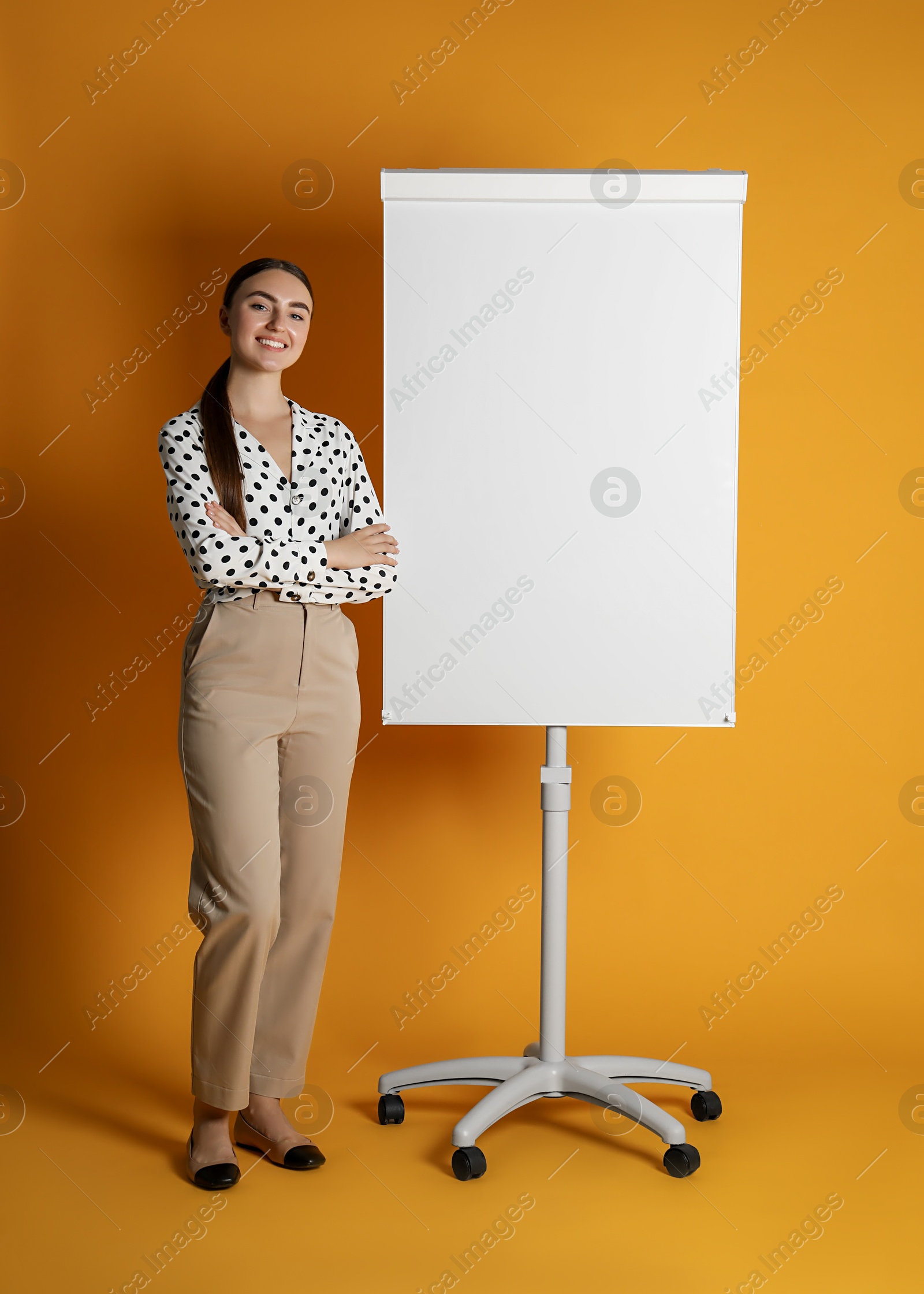 Photo of Happy woman near flip chart on orange background. Mockup for design