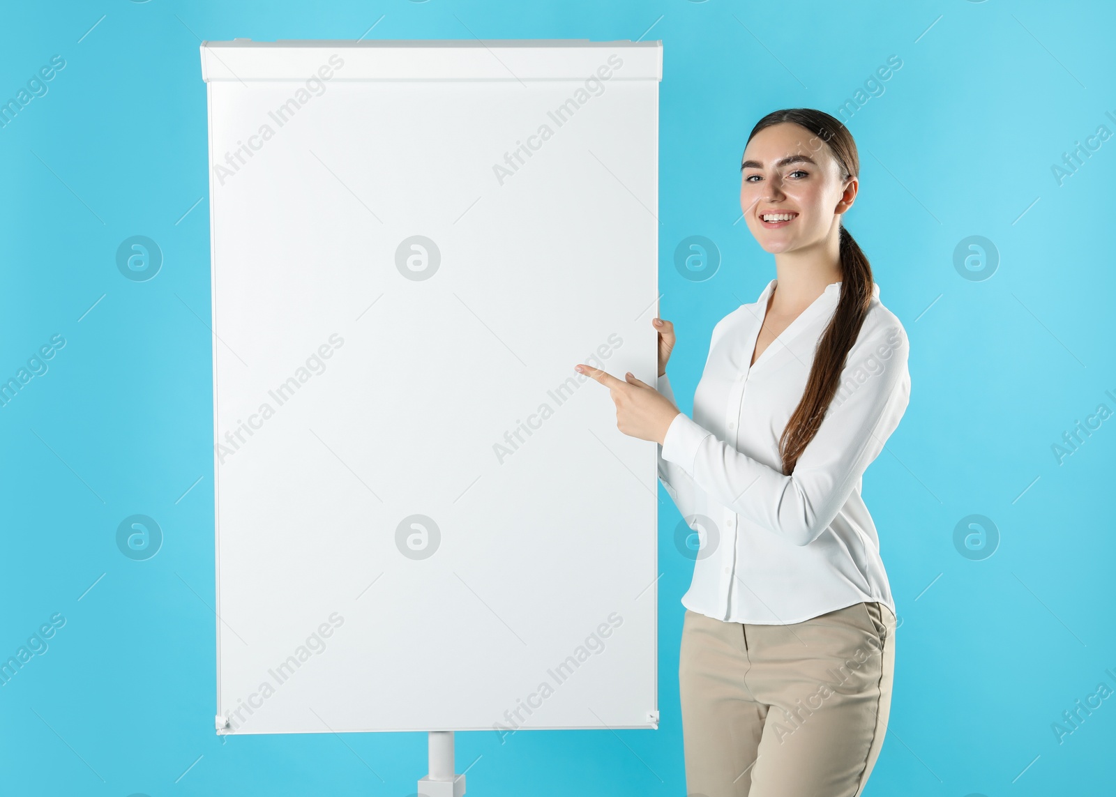 Photo of Happy woman near flip chart on light blue background. Mockup for design