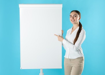 Photo of Happy woman near flip chart on light blue background. Mockup for design