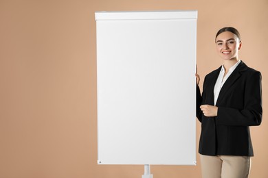 Photo of Happy woman near flip chart on pale brown background. Mockup for design