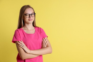 Photo of Portrait of teenage girl in glasses on yellow background, space for text