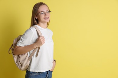 Photo of Teenage girl with backpack on yellow background, space for text