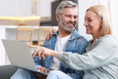 Happy middle aged couple using laptop on sofa indoors