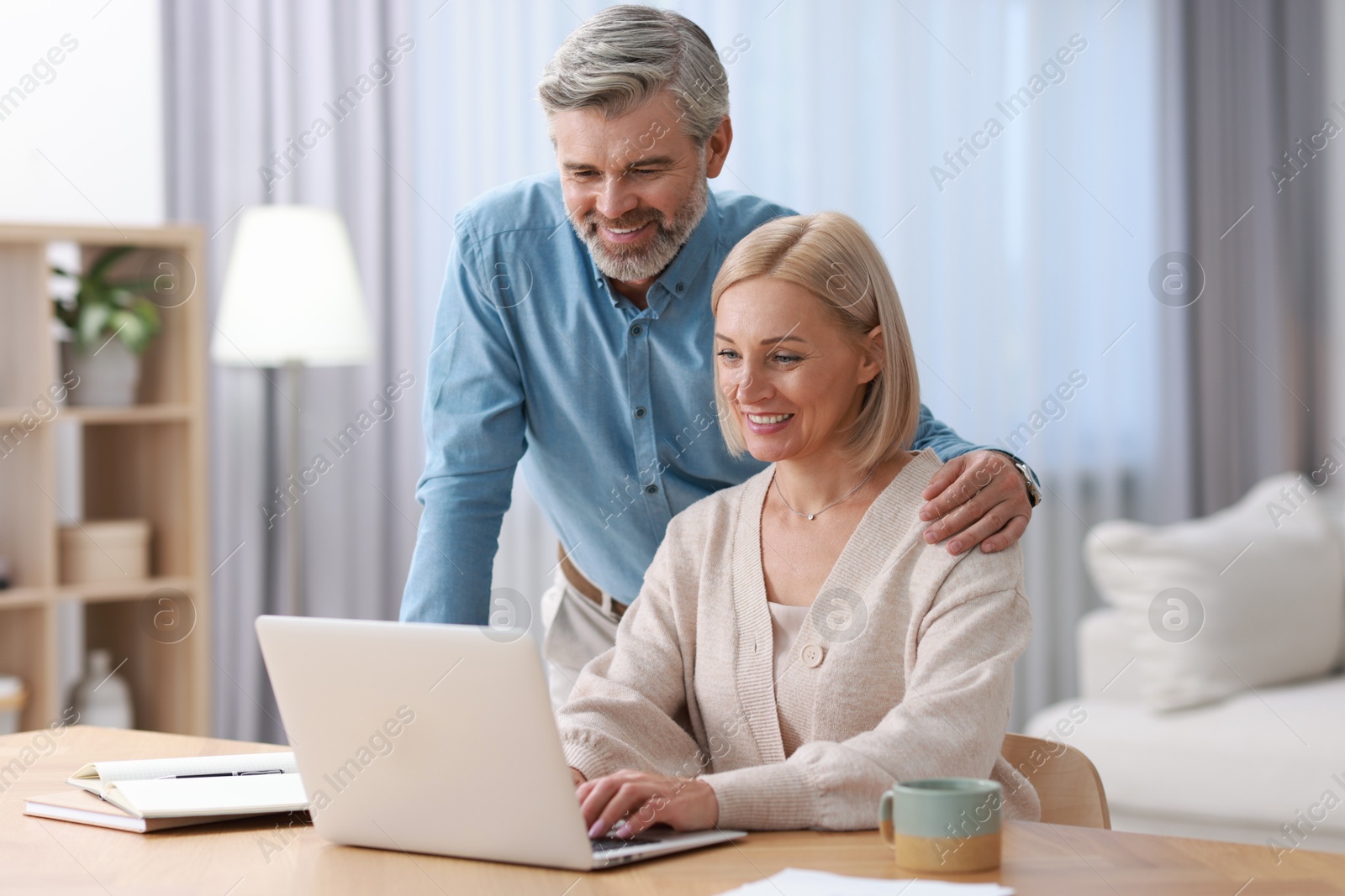 Photo of Happy middle aged couple working with laptop at table indoors