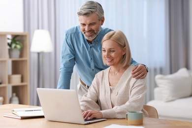 Photo of Happy middle aged couple working with laptop at table indoors