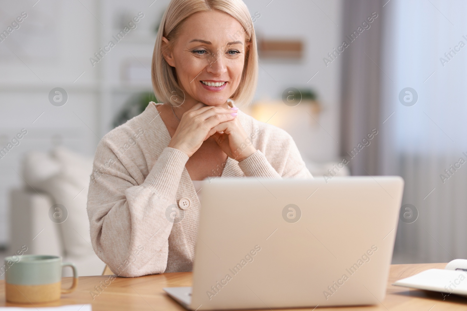 Photo of Happy middle aged woman using laptop at table indoors