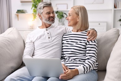 Photo of Happy middle aged couple using laptop on sofa at home