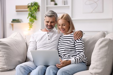 Happy middle aged couple using laptop on sofa at home