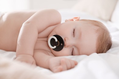 Cute little baby with pacifier sleeping on bed at home