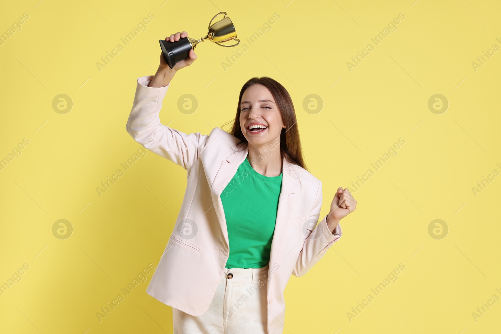 Photo of Happy winner with gold trophy cup on yellow background