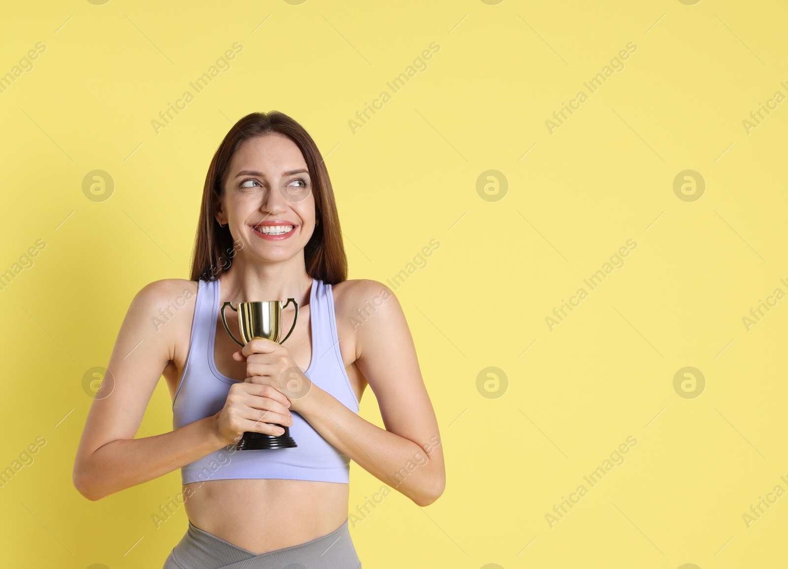 Photo of Happy winner with gold trophy cup on yellow background, space for text