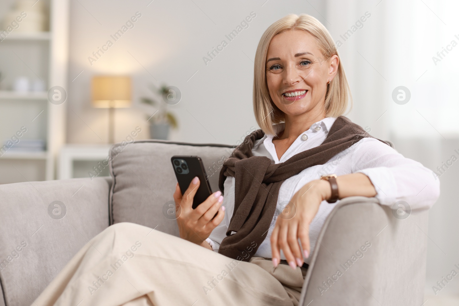 Photo of Smiling middle aged woman with smartphone on armchair at home