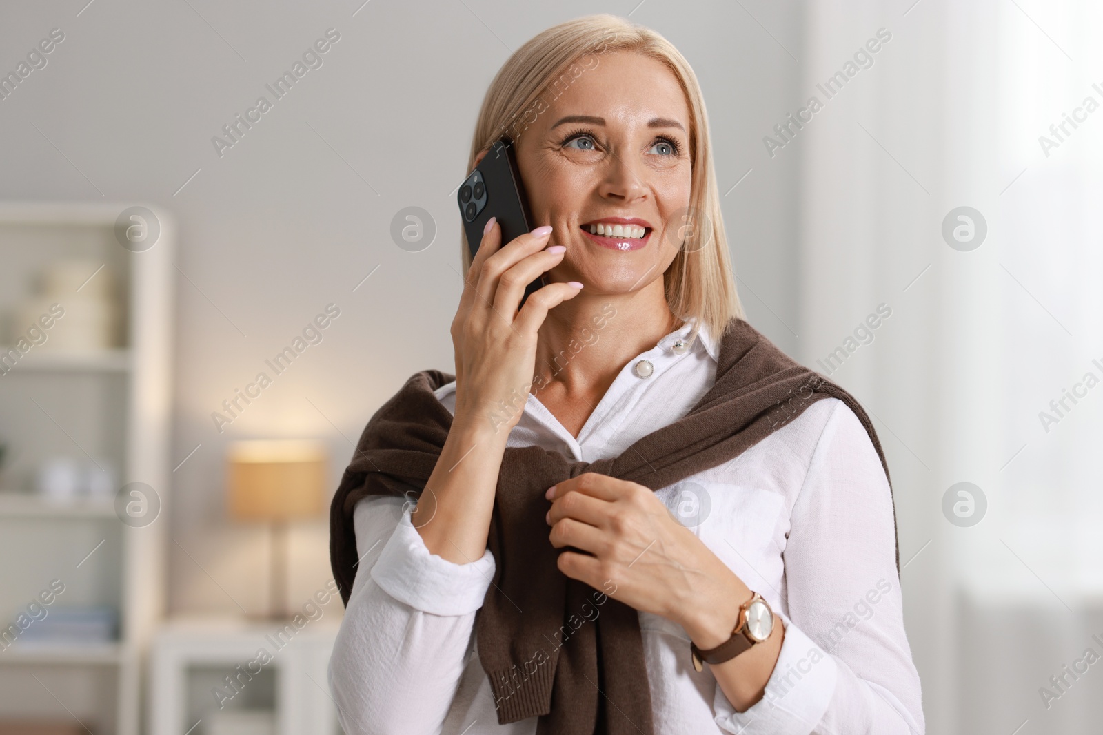 Photo of Smiling middle aged woman talking by smartphone at home