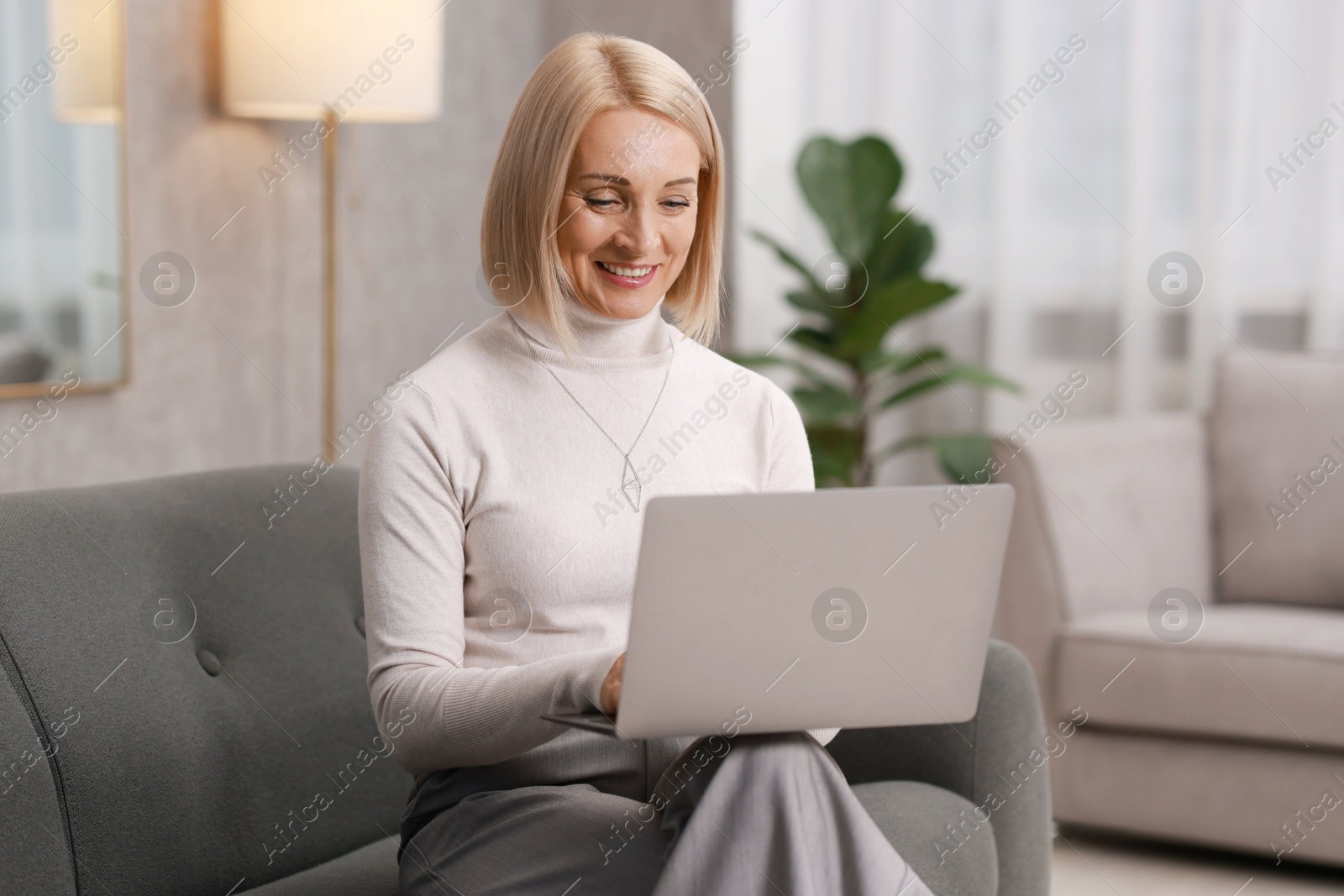 Photo of Smiling middle aged woman working with laptop on sofa at home