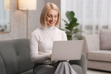 Smiling middle aged woman working with laptop on sofa at home