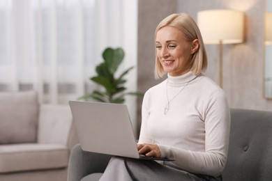 Photo of Smiling middle aged woman working with laptop on sofa at home