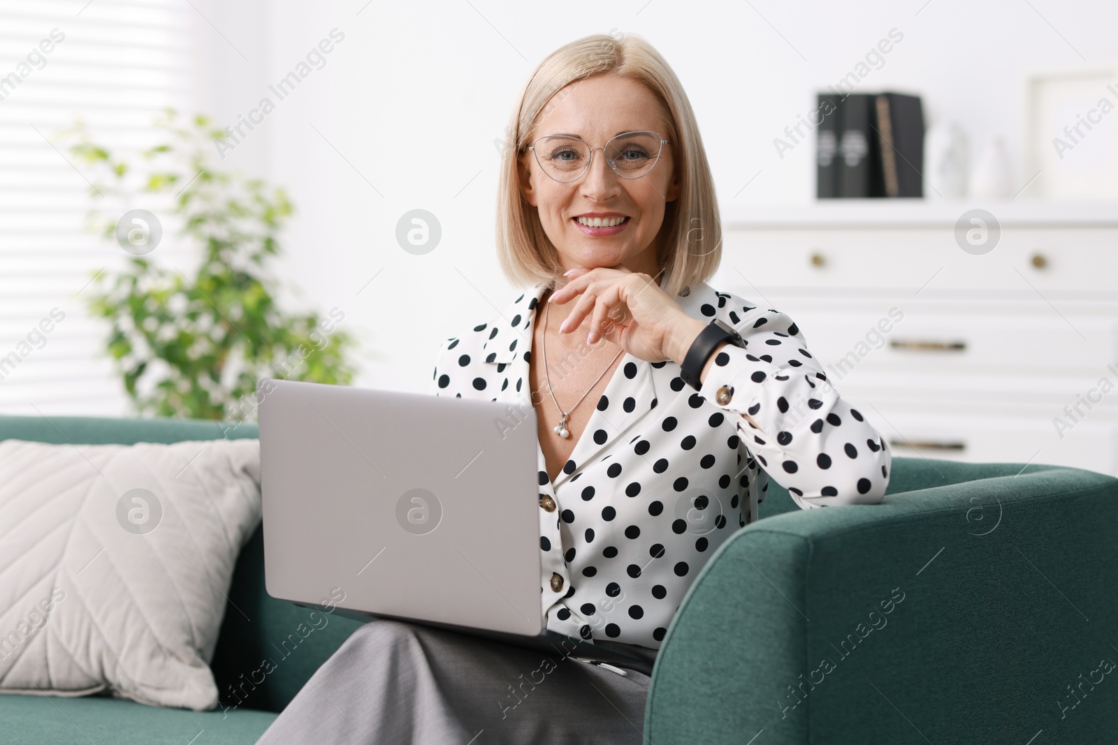 Photo of Smiling middle aged woman working with laptop on sofa at home