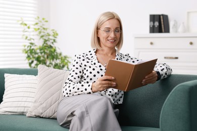 Photo of Portrait of smiling middle aged woman reading book on sofa at home