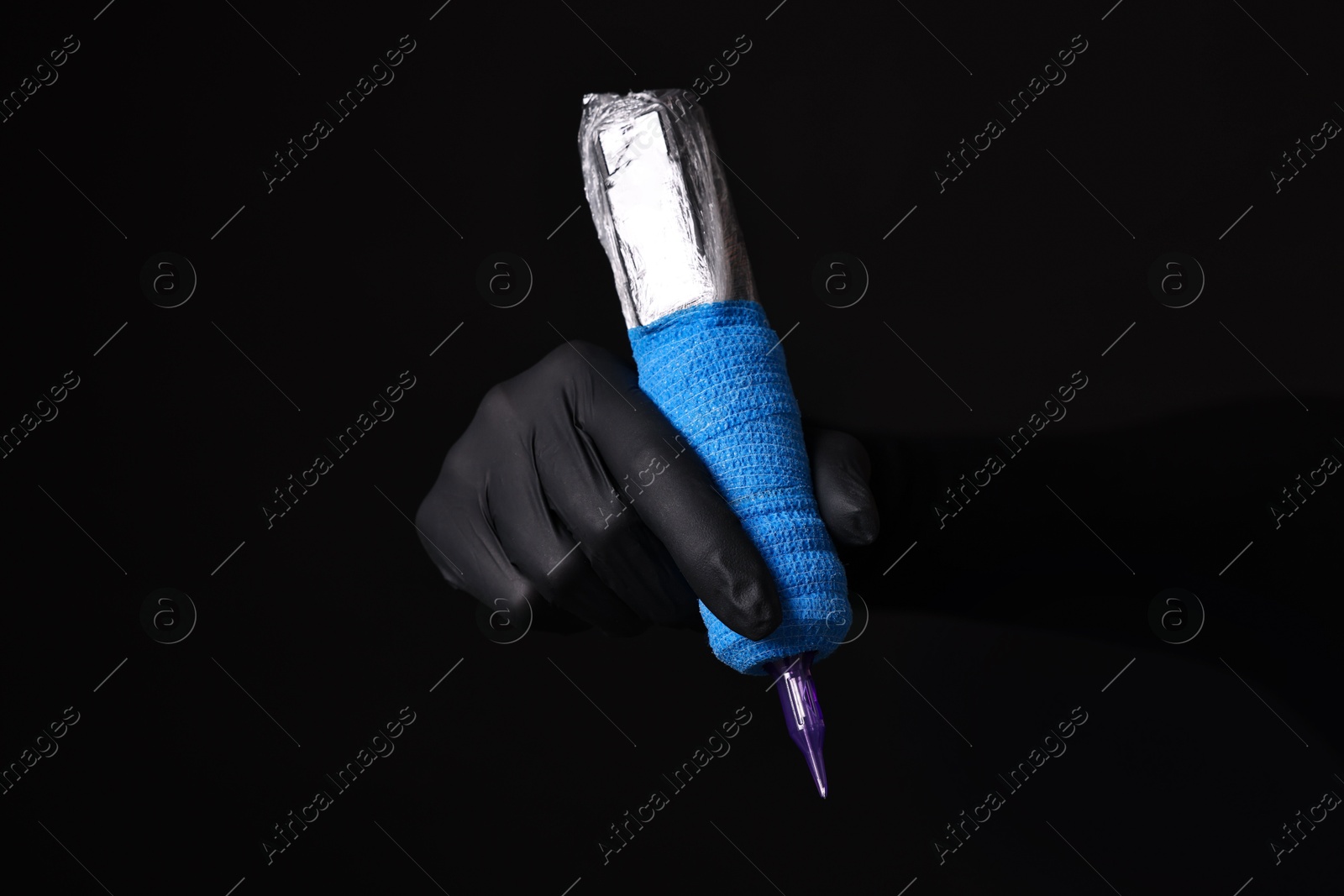 Photo of Professional artist in gloves holding tattoo machine on black background, closeup