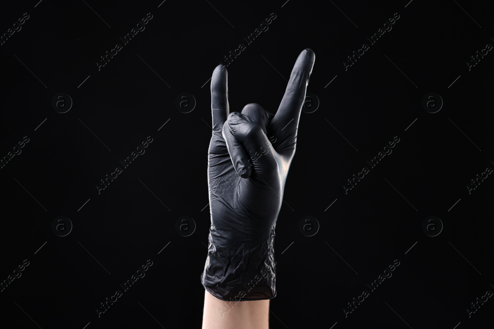 Photo of Man in latex glove showing rock gesture on black background, closeup