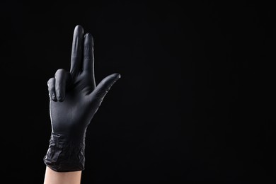 Photo of Man in latex glove showing three fingers on black background, closeup. Space for text