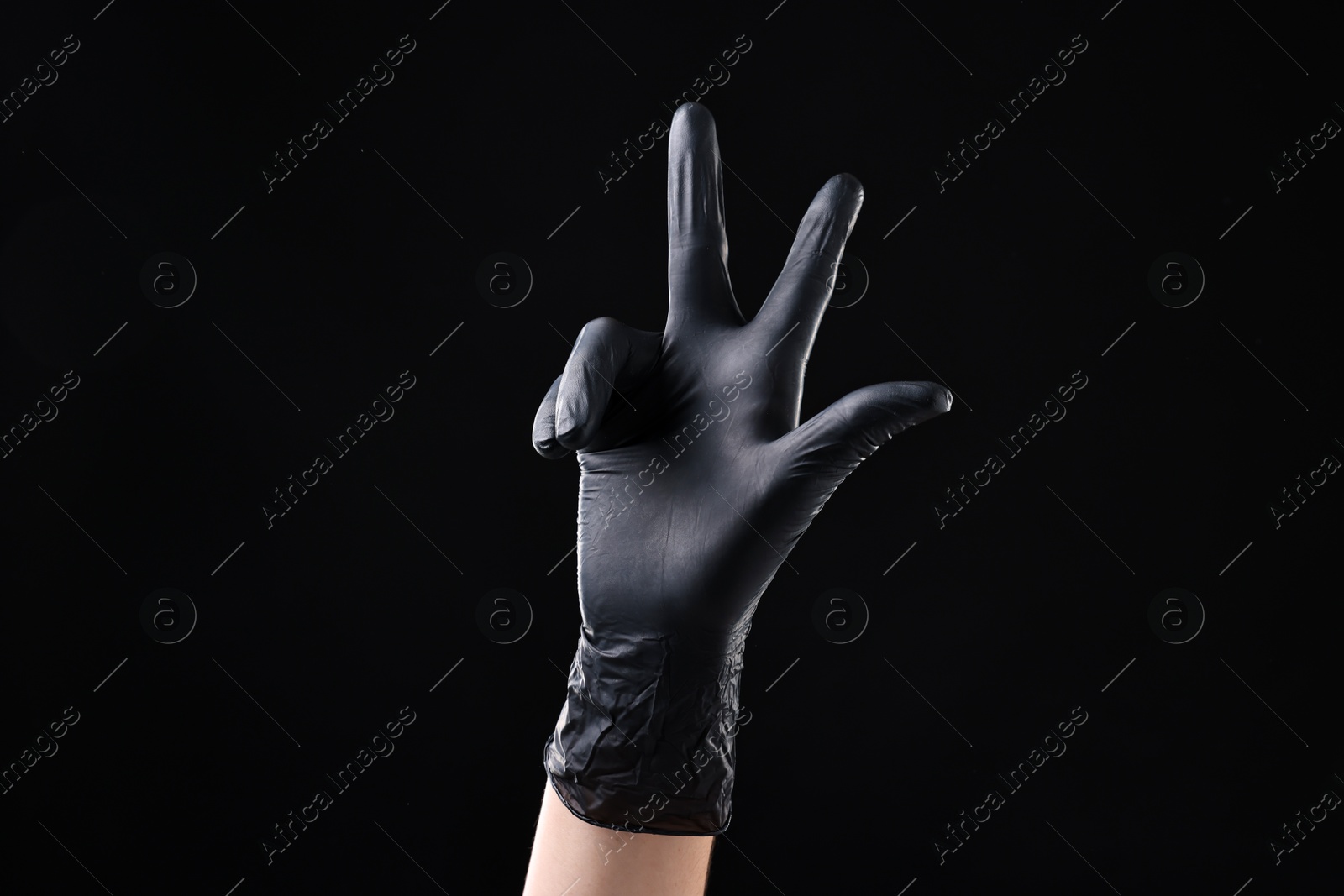 Photo of Man in latex glove showing three fingers on black background, closeup