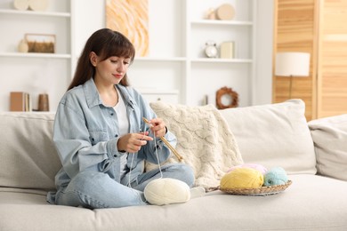 Beautiful woman knitting on sofa at home