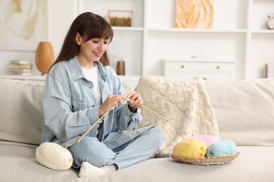 Beautiful woman knitting on sofa at home