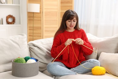 Beautiful woman knitting on sofa at home