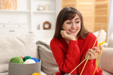 Photo of Beautiful woman with colorful yarns and knitting needles on sofa at home