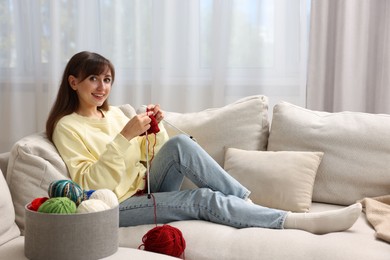 Beautiful woman knitting on sofa at home