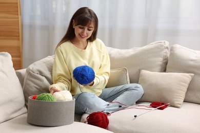 Beautiful woman with colorful yarns and knitting needles on sofa at home