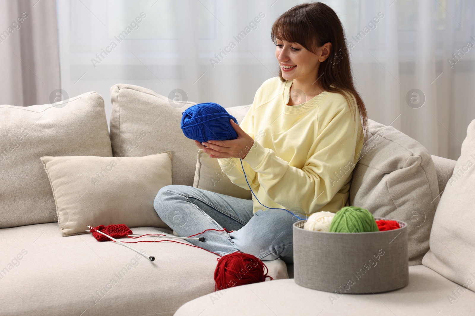 Photo of Beautiful woman with colorful yarns and knitting needles on sofa at home