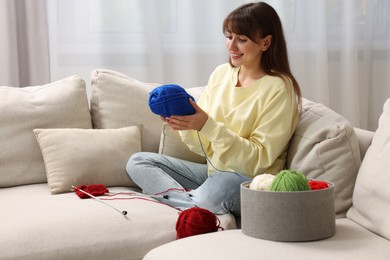 Beautiful woman with colorful yarns and knitting needles on sofa at home