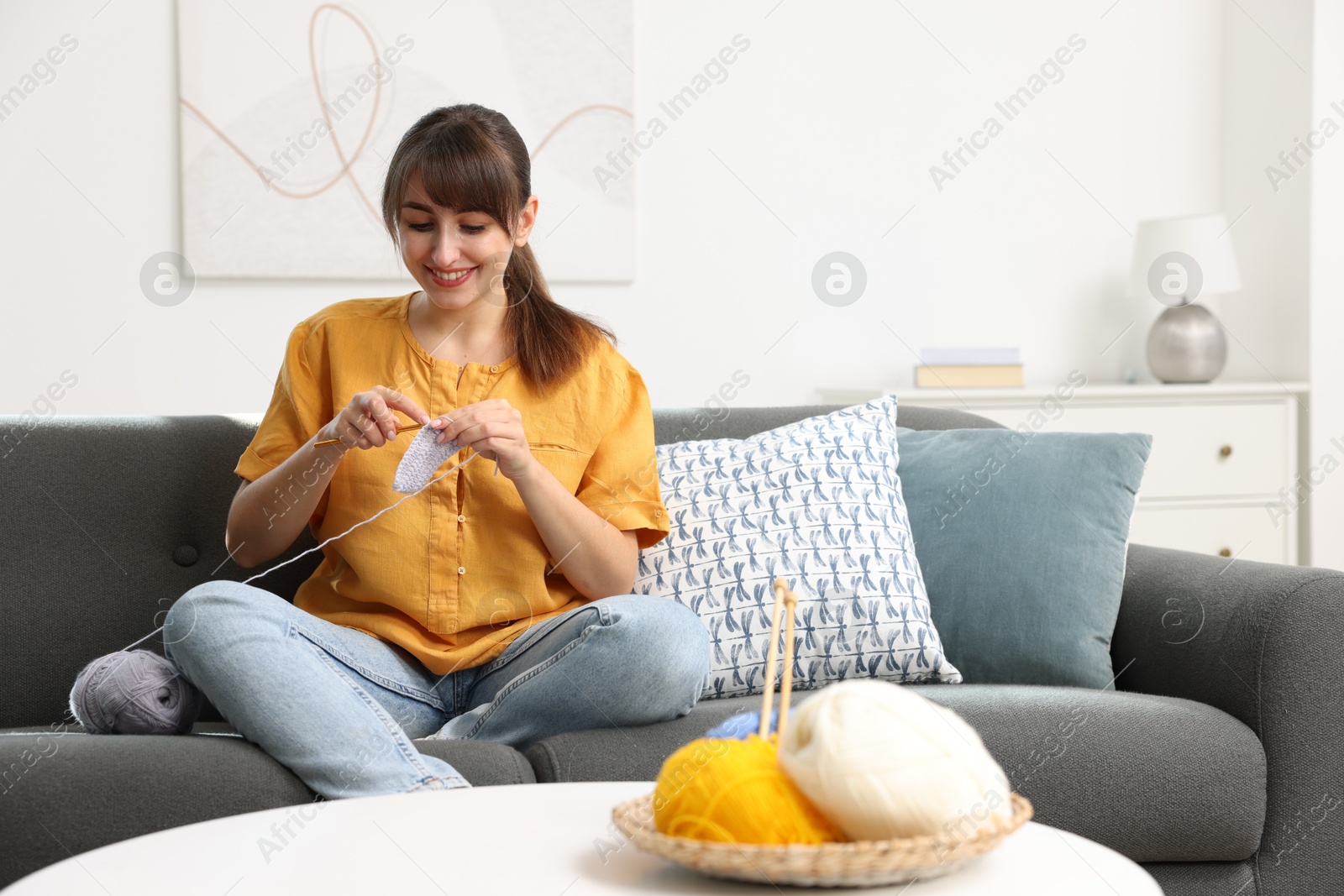 Photo of Beautiful woman crocheting with hook on sofa at home