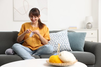 Beautiful woman crocheting with hook on sofa at home