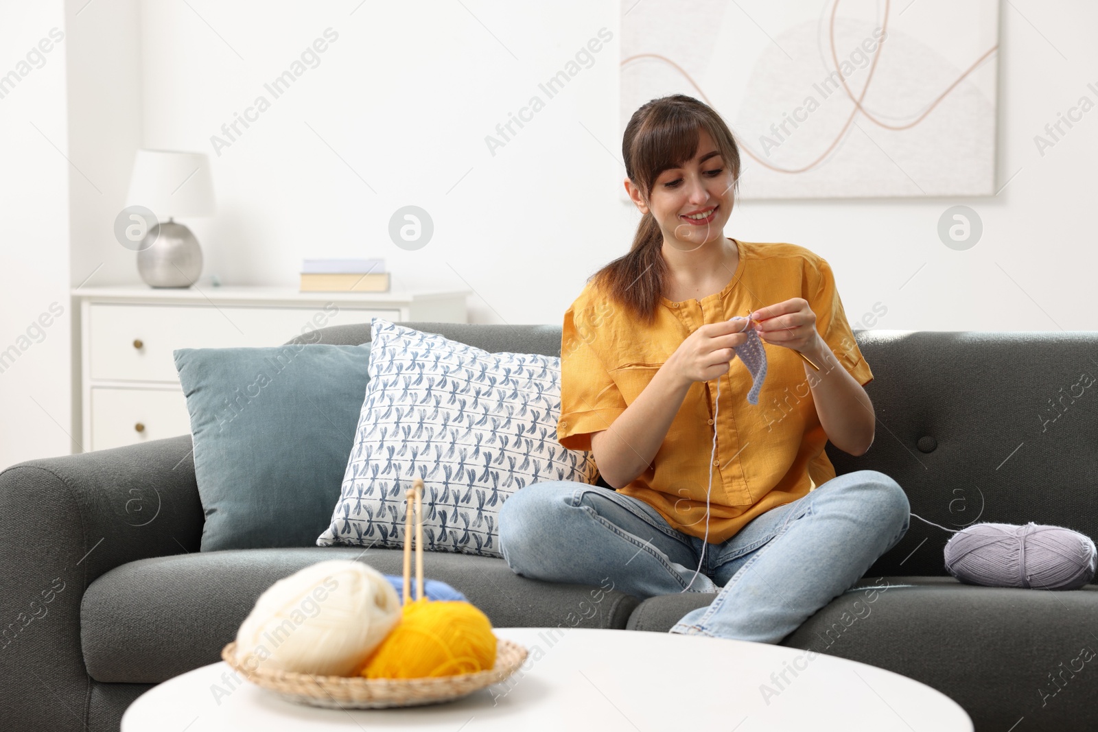 Photo of Beautiful woman crocheting with hook on sofa at home