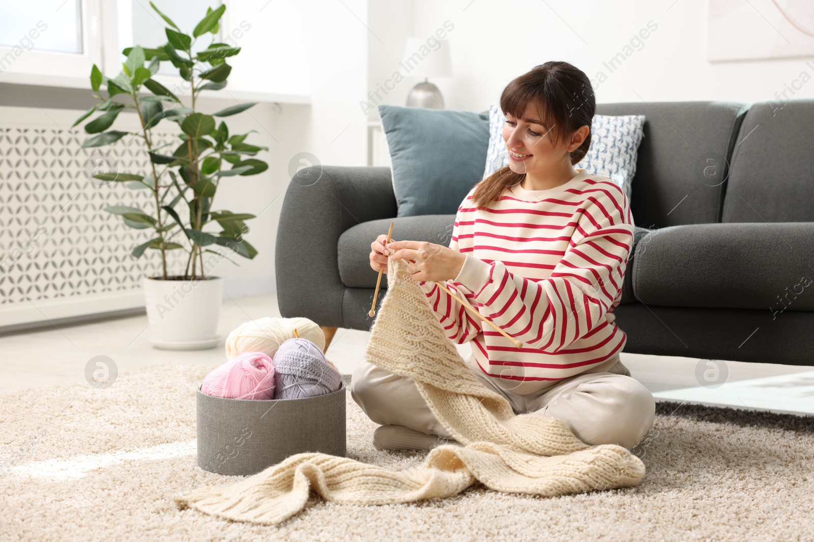 Photo of Beautiful woman knitting with needles on floor at home