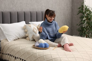 Beautiful woman with colorful yarns on bed at home. Knitting material