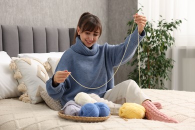 Photo of Beautiful woman with colorful yarns on bed at home. Knitting material