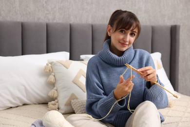 Beautiful woman knitting with needles on bed at home