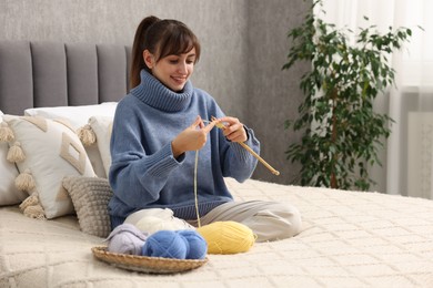 Beautiful woman knitting with needles on bed at home