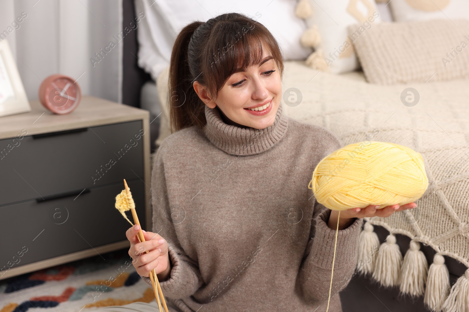 Photo of Beautiful woman with yellow yarn and knitting needles on floor at home